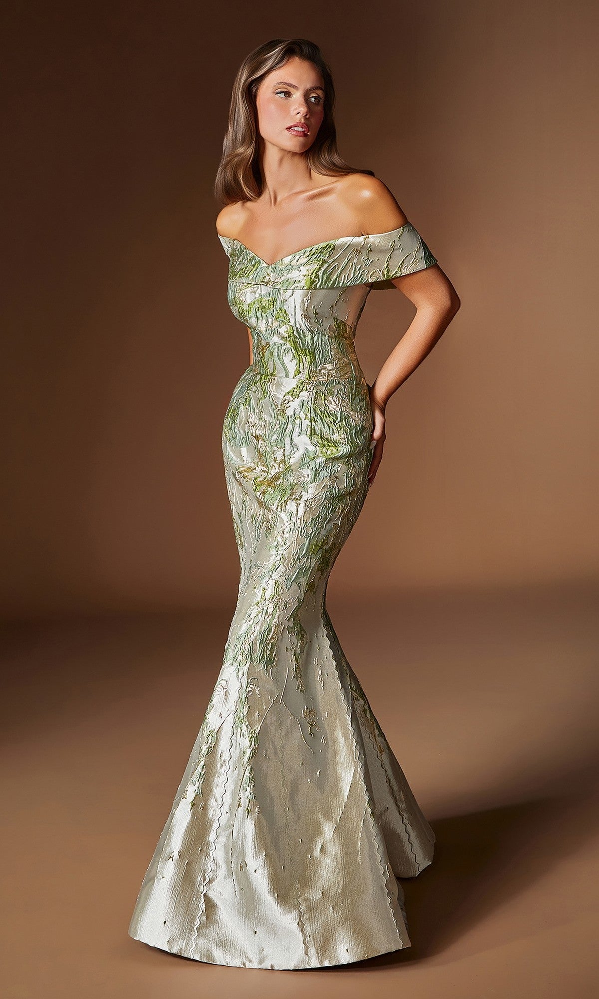 A woman wears the Ladivine CD0107, a fitted green formal dress with an off-the-shoulder design, metallic sheen, and mermaid silhouette featuring a flared hem, as she stands against a plain brown background.